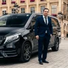 Photo d'un chauffeur vtc à caen en costume devant son véhicule haut de gamme noir